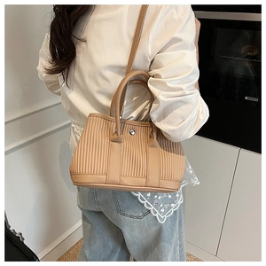Model wearing a pleated camel bucket bag with metallic ring clasp and shoulder strap