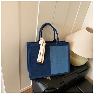 Close-up of stylish blue denim tote bag with two-tone patchwork and decorative ribbon detail