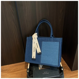 Detailed texture of two-tone denim patchwork tote bag with decorative brand ribbon