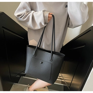 Close-up of minimalist black pebble leather tote bag featuring a front pocket and metal snap