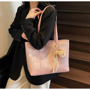 Pink matte leather tote bag with plush bear charm worn by model on dark stairs
