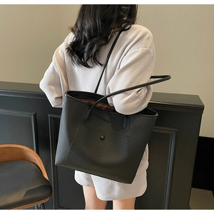 Detail view of large black leather tote bag featuring a textured pebbled finish and front pocket