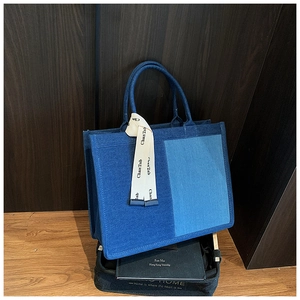 Detailed close-up of a two-tone denim tote bag featuring vertical stitching and a silk ribbon