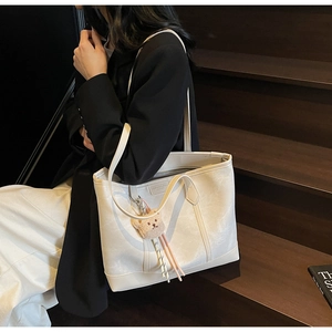 Close-up of beige tote bag with cute bear charm and fashion leather patch detail
