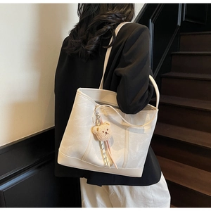 Detailed side view of off-white tote bag with teddy bear pendant on shoulder of a model