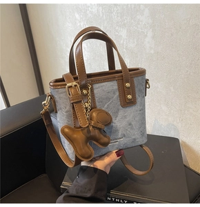 Detail of blue denim bucket bag with brown leather handles and puppy charm