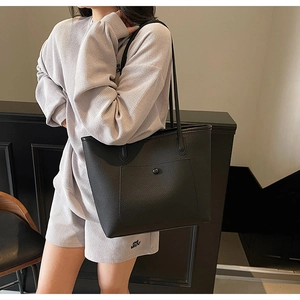 Detail of black pebbled leather tote bag featuring a front pocket and metallic snap button