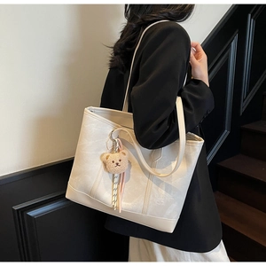 Model showing cream tote bag with bear charm on minimalist wooden staircase