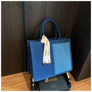 Detailed macro view of two-tone denim tote bag featuring blue patchwork and logo ribbon