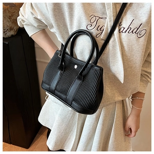 Close-up of black pleated bucket bag with dual handles and slender crossbody strap
