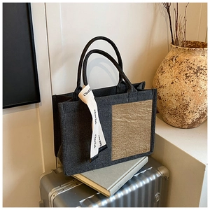 Detailed view of dark grey canvas tote bag with brown contrast panel and decorative ribbon