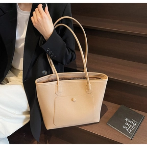 Detail of khaki pebbled leather tote bag featuring front pocket on wooden stairs