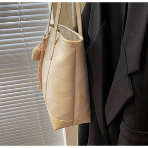 Detail of off-white leather tote bag featuring stylish plush ball and braided rope pendant
