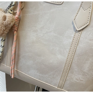 Detail of cream white tote bag featuring natural pleated texture and a cute plush bear charm