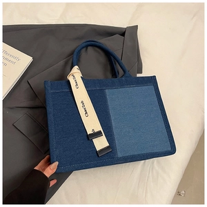 Close-up of blue patchwork denim tote bag with branded woven strap detail and handles
