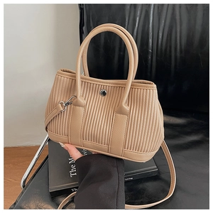 Detail of khaki pleated bucket bag with silver hardware and dual handles on books