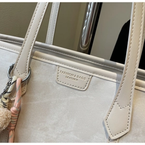 Detail of off-white tote bag showing leather texture, stitching, and plush charm