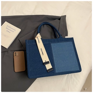 Detail of blue patchwork denim tote bag with decorative strap on white bedding