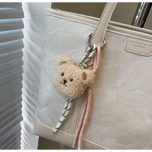 Close-up of a cute plush bear pendant with colorful braided rope on a white tote bag