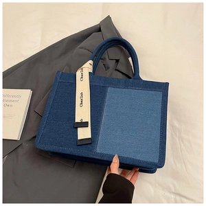 Close-up of two-tone denim tote bag with decorative textile ribbon and handle detail
