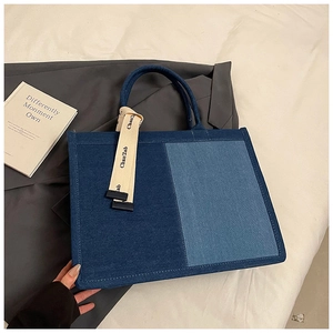 Close-up of dual-tone blue denim tote bag featuring decorative branded webbing straps