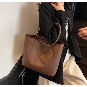 Detail of a large brown pebbled leather tote bag worn by a model in office attire