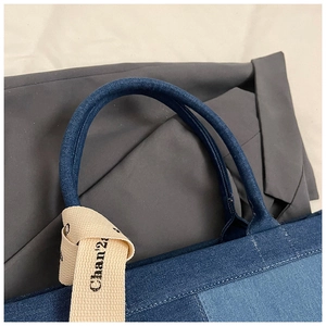 Detailed close-up of the denim tote bag handle with embroidered Chan'22 artistic text