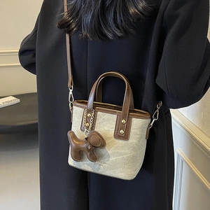 Canvas bucket bag with brown leather trim and cute puppy charm shown on a shoulder