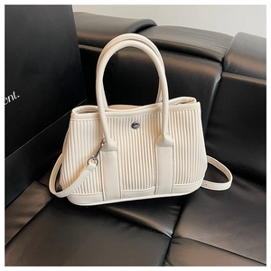 Detail of off-white pleated tote bag with vertical texture and metal snap on leather sofa