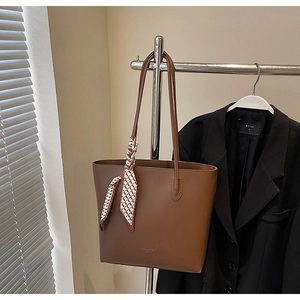 Brown leather tote bag with decorative geometric scarf hanging on a sleek metal display stand