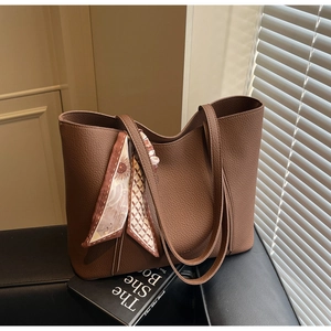 Close-up of brown lychee grain leather tote bag with silk scarf on a luxury sofa