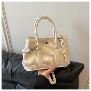 Close-up of cream textured bucket bag showing vertical pleats and detachable shoulder strap
