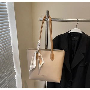 Detail of beige tote bag with brown straps and houndstooth silk scarf on metal hanger