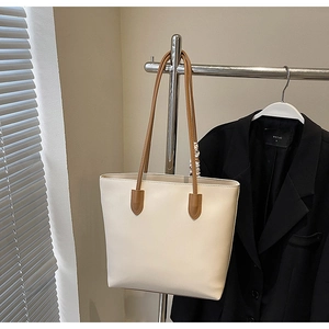 Detail view of a cream white tote bag with brown handles hanging in an office setting