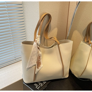Large beige tote bag with brown handles and a decorative silk scarf near a sunny window