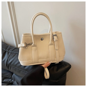 Close-up of cream pleated bucket bag showing vertical textured fabric and metal buckles