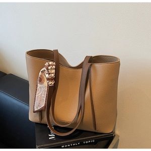 Detail of khaki pebbled leather tote bag featuring brown handles and decorative silk scarf