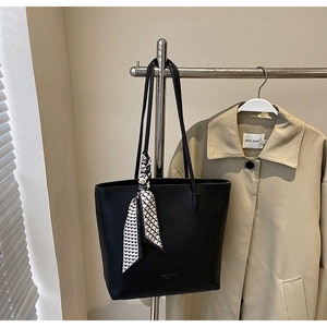 Close-up of black tote bag with geometric silk scarf detail on a fashion studio rack