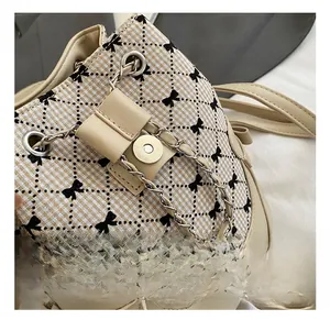 Detail of metal magnetic buckle and chain on beige plaid backpack with black bow embroidery