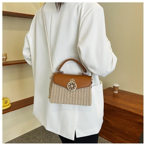 Detail of woven straw crossbody bag with metal crown accent and thick rope shoulder strap