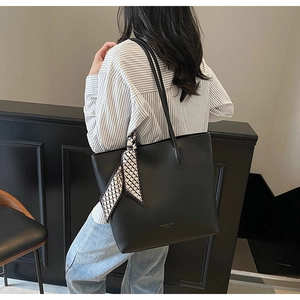 Detail of black leather tote bag with silk scarf accessory and gold fashion lettering