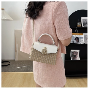 Detail of a straw woven box bag with white leather flap and golden crown hardware buckle