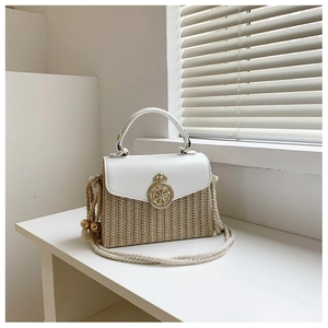 Close-up of woven straw handbag with white leather trim and gold crown buckle detail