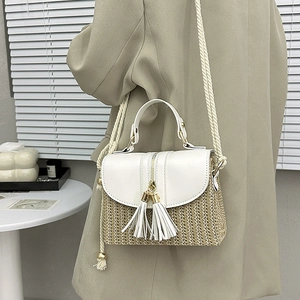 Detail of woven straw bag featuring white leather flap and dual tassel decorative pendants