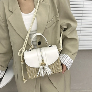 Detail of woven straw handbag with white leather trim and decorative double tassels