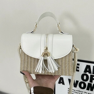 Detail of straw handbag with white leather flap, gold tassels, and woven rope strap