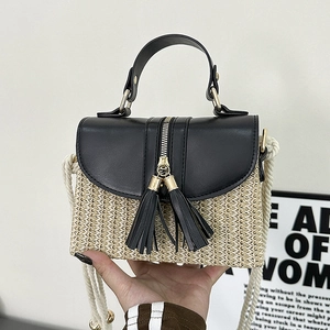 Close-up of straw woven bag with black leather flap, dual metal zippers and fringe tassels