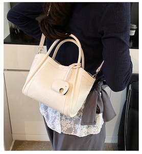 Detail view of cream white pebbled leather bucket bag with an elephant charm and crossbody strap
