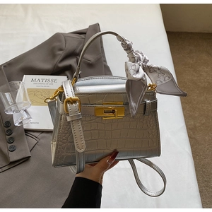 Détail d'un sac argenté motif crocodile avec fermoir doré et accessoire de foulard