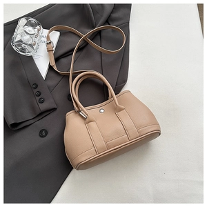 Close-up of beige pleated bucket bag with silver metal buckle on a grey suit jacket